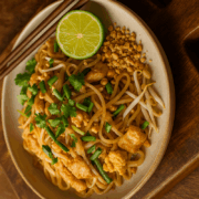 Fertiges Pad Thai mit Reisnudeln, Ei, Hähnchen, Limette und Erdnüssen auf Teller