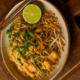 Fertiges Pad Thai mit Reisnudeln, Ei, Hähnchen, Limette und Erdnüssen auf Teller